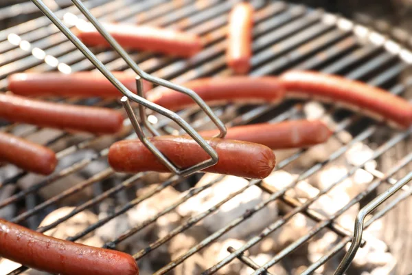 Pinças segurando linguiça — Fotografia de Stock