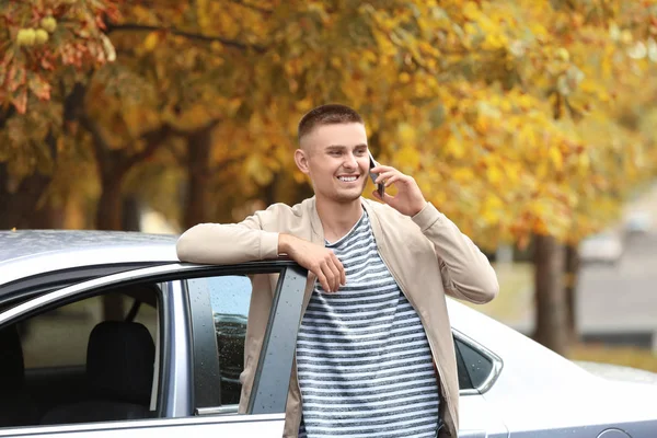 Красивый молодой человек разговаривает по мобильному телефону возле машины в парке — стоковое фото