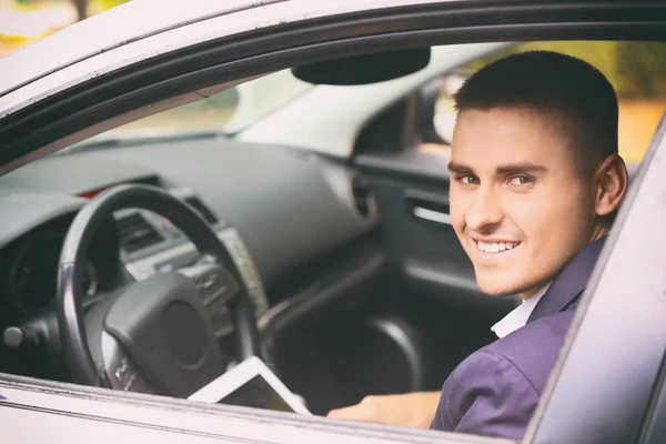 Joven hombre de negocios guapo usando tableta de computadora en coche moderno —  Fotos de Stock