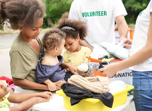 Voluntarios compartiendo ropa y juguetes con niños africanos pobres al aire libre — Foto de Stock