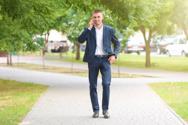Parkta yürürken cep telefonu üzerinde konuşurken yakışıklı genç işadamı