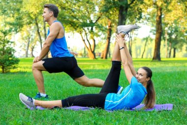 Young sporty couple doing exercises in green park clipart