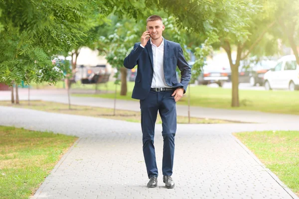Guapo joven hombre de negocios hablando por teléfono móvil mientras camina en el parque —  Fotos de Stock