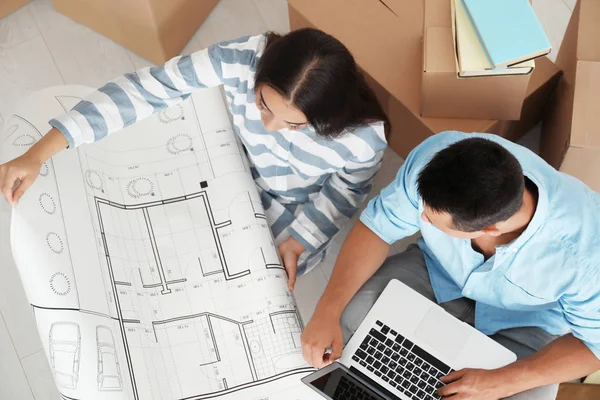 Feliz joven pareja sentada en el suelo con el ordenador portátil y el dibujo de su nuevo apartamento — Foto de Stock