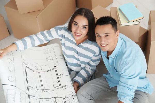 Šťastný mladý pár sedící na podlaze s výkresem svého nového bytu — Stock fotografie