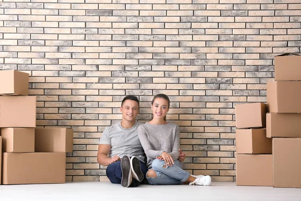 Happy young couple and moving boxes near brick wall