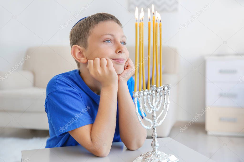 Jewish boy looking at flame of candles in menorah, indoors