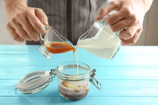 Wanita menuangkan yogurt dan saus karamel ke dalam toples kaca — Stok Foto