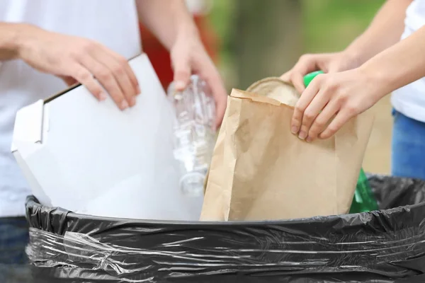 Pareja joven arrojando basura al cubo de basura al aire libre, primer plano —  Fotos de Stock