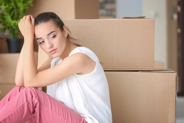 Уставшая молодая женщина, сидящая на полу в своей новой квартире рядом с коробками — стоковое фото