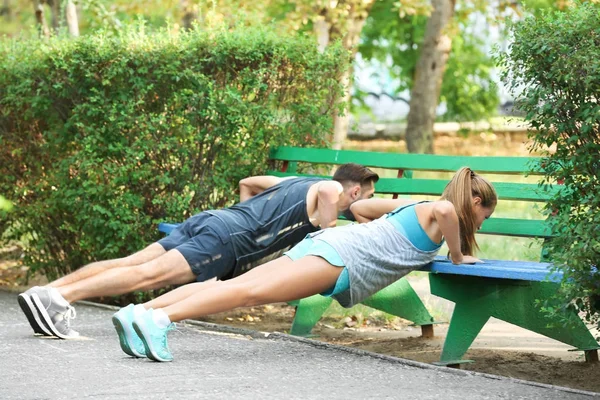 Young man and woman doing exercises in park — Stock Photo, Image