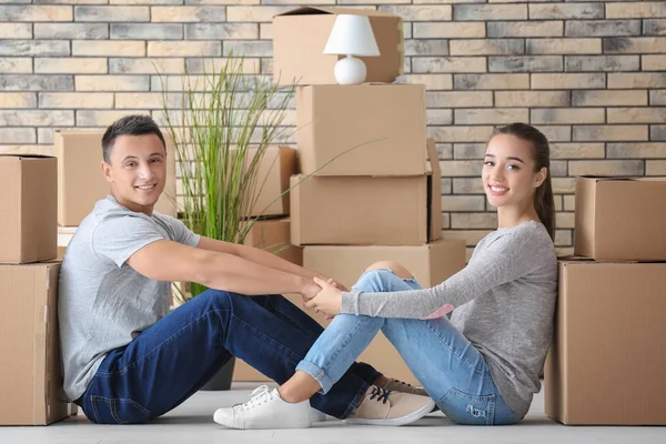 Gelukkige jonge paar zittend op de vloer in hun nieuwe appartement in de buurt van Verhuisdozen — Stockfoto