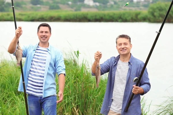 Dos pescadores sosteniendo pescado recién capturado en la orilla del río — Foto de Stock