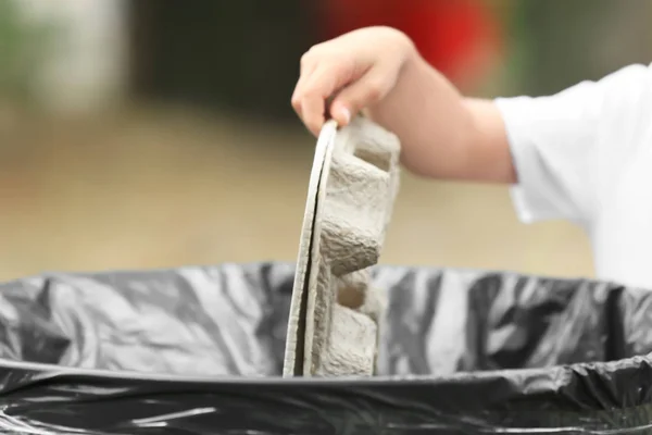 Рука ребенка выбрасывает мусор в мусорный бак на открытом воздухе — стоковое фото