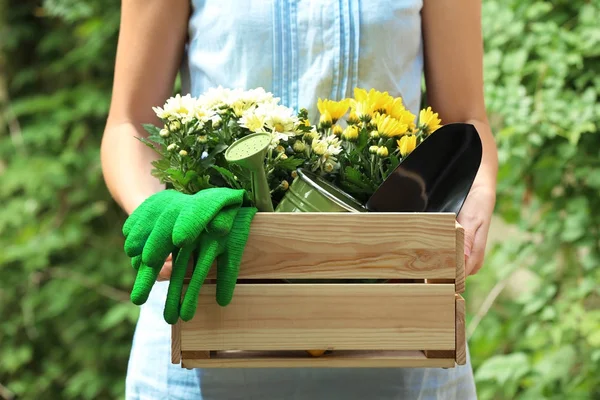 Donna che tiene scatola di legno con attrezzi da giardinaggio e piante all'aperto — Foto Stock
