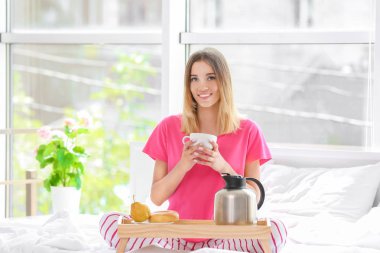 Genç bir kadın sabahları yatakta kahvaltı yapıyor.