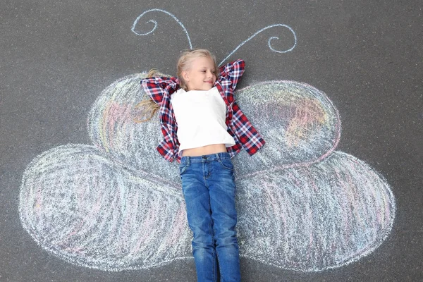 Little girl lying on chalk drawing of butterfly outdoors — Stock Photo, Image