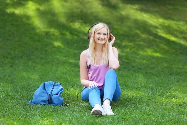 Gyönyörű fiatal nő, zenét hallgatni, miközben ül a gyep a parkban — Stock Fotó