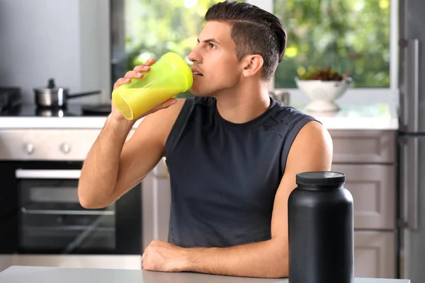 Молодой человек пьет протеиновый коктейль на кухне — стоковое фото