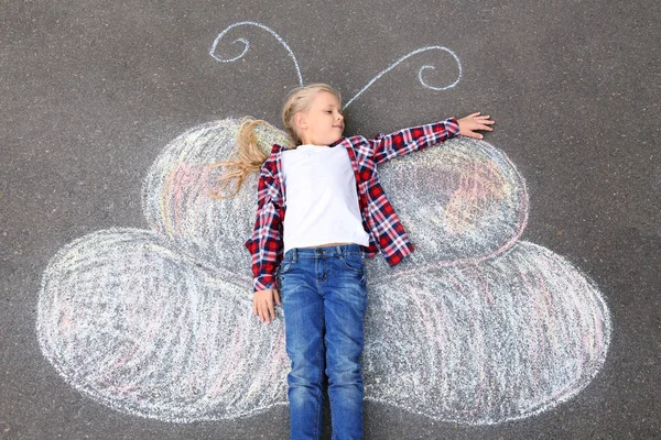 Little girl lying on chalk drawing of butterfly outdoors — Stock Photo, Image