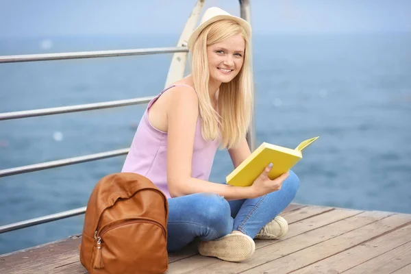 Gyönyörű fiatal nő könyvével ülve Pier — Stock Fotó