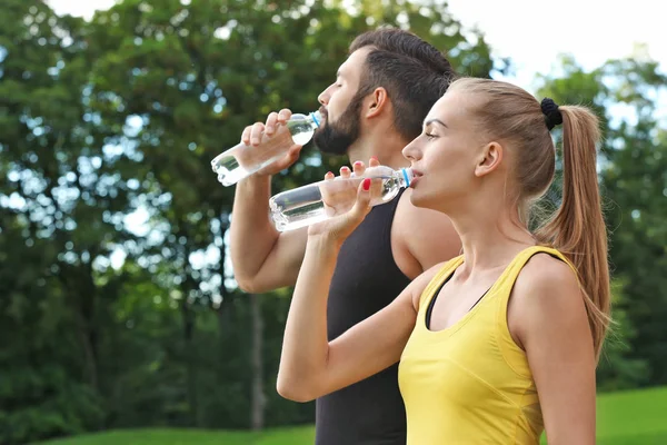 Joven pareja deportiva bebiendo agua en parque verde —  Fotos de Stock