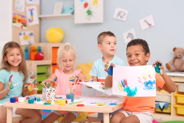 Niedliche Kinder malen mit ihren Handflächen am Tisch drinnen — Stockfoto
