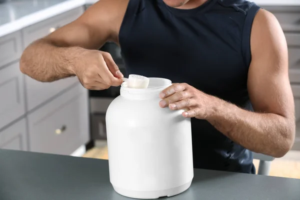 Man holding plastic scoop with protein powder indoors — Stock Photo, Image