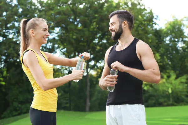Jong sportief stel met flessen water in groen park — Stockfoto