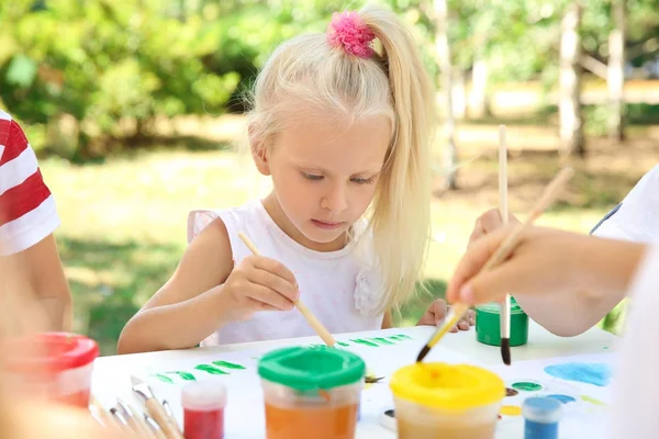 Маленькая девочка рисует на открытом воздухе вместе с друзьями — стоковое фото
