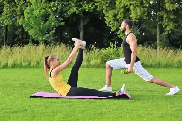 Young sporty couple doing exercises in green park — Stock Photo, Image