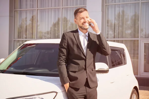 Продавец говорит по телефону возле нового автомобиля на открытом воздухе — стоковое фото
