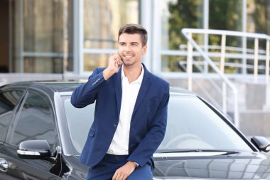 Genç işadamı car yakınındaki telefonda konuşuyor