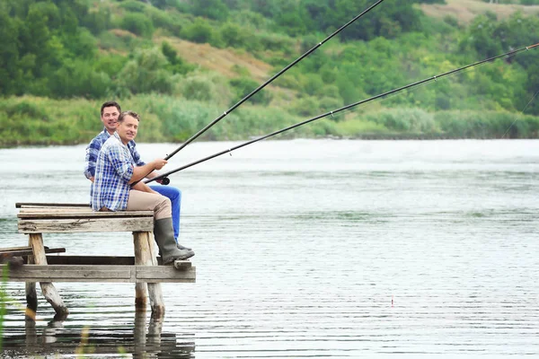 Dos hombres pescando desde el muelle en el río — Foto de Stock