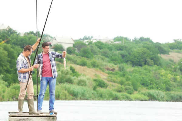 Dos pescadores sosteniendo peces recién capturados en el río — Foto de Stock