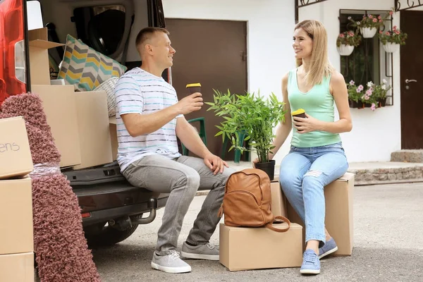 Pareja feliz con cajas móviles bebiendo café cerca del coche — Foto de Stock