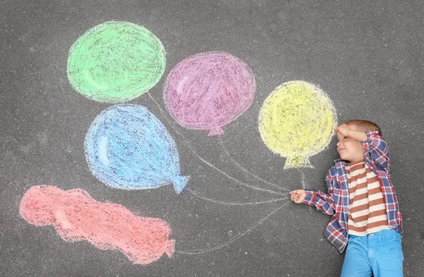 Liten pojke ligger nära krita ritning av luftballonger på asfalt — Stockfoto
