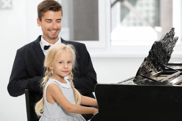 Маленькая девочка и молодой человек играют на пианино — стоковое фото