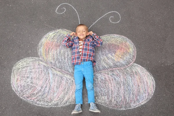 Маленький мальчик лежит на мелом рисунке бабочки на открытом воздухе — стоковое фото