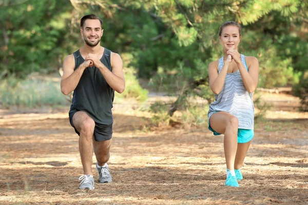 Young man and woman doing exercises in park — Stock Photo, Image