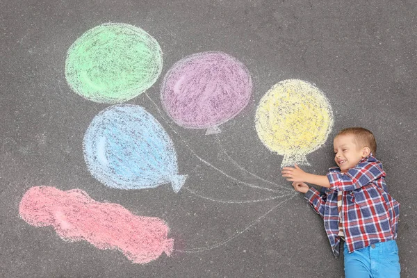 Liten pojke ligger nära krita ritning av luftballonger på asfalt — Stockfoto