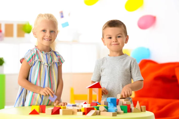 Niedliche Kinder spielen mit Bauklötzen auf Tisch drinnen — Stockfoto