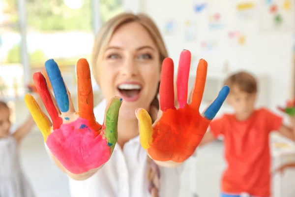 Jonge vrouwelijke kunst leraar met handen in verf binnenshuis — Stockfoto
