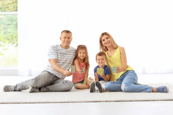 Familia feliz con la palabra HOME sentado en el piso en el nuevo apartamento —  Fotos de Stock