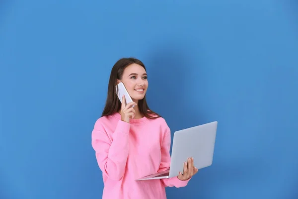 Молода леді з ноутбуком розмовляє по телефону проти кольорової стіни — стокове фото
