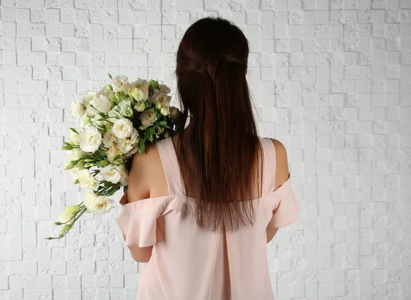 Frau hält Strauß schöner Eustoma-Blumen auf Backstein-Hintergrund — Stockfoto