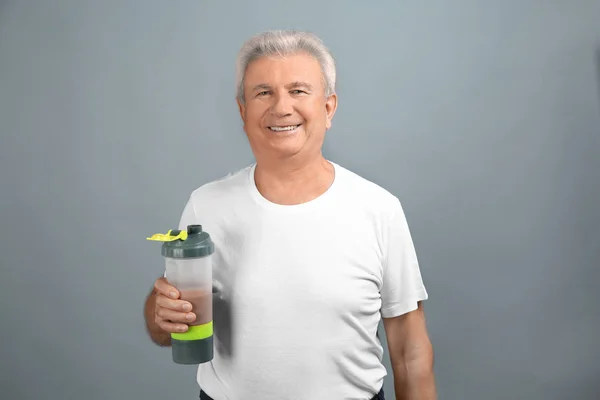 Спортивный пожилой человек с протеиновым коктейлем на цветном фоне — стоковое фото