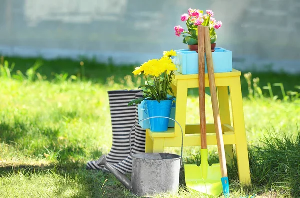 Composición con hermosas flores, botas de goma y herramientas de jardinería en el patio trasero — Foto de Stock