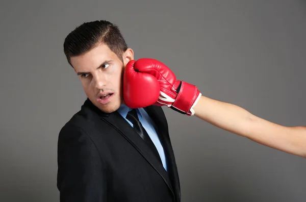 Рука женщины в боксёрской перчатке бьет бизнесмена на сером фоне — стоковое фото
