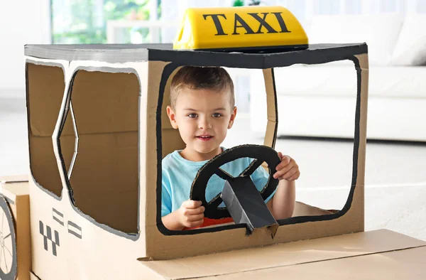 Little boy playing with cardboard taxi in light room — Stock Photo, Image